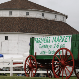 Historical White Round Barn with a Green Wagon with Red Wheels with a sign that says 