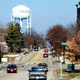 Cars Driving Road Through Town with Large White Water Tower in the Background for 